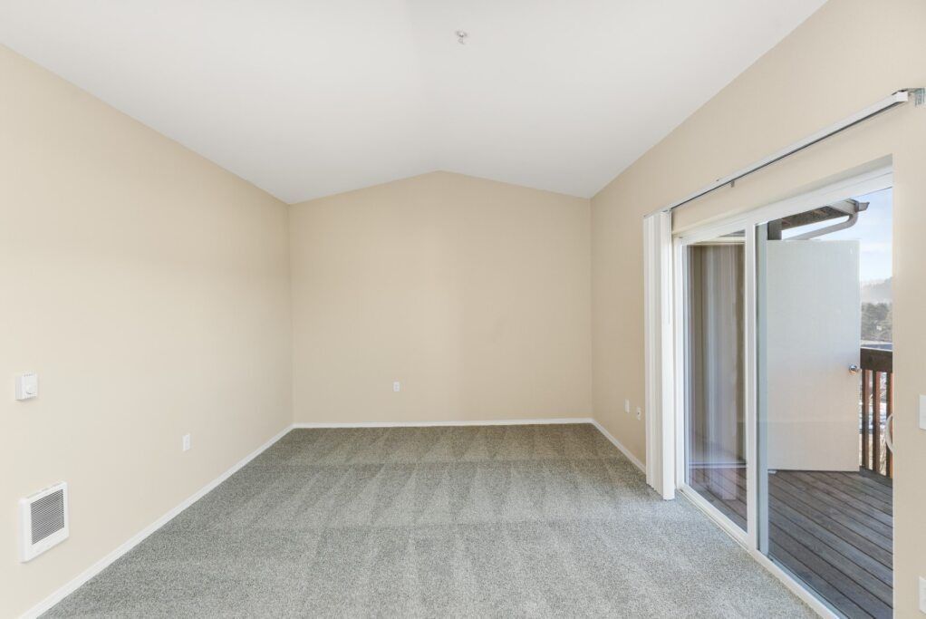 Empty beige room with gray carpet and sliding glass door to a balcony