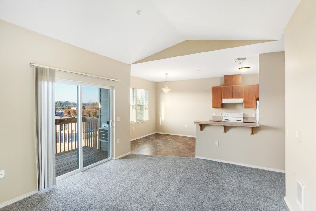 Empty living room with sliding glass doors, carpet, and a view into the kitchen area