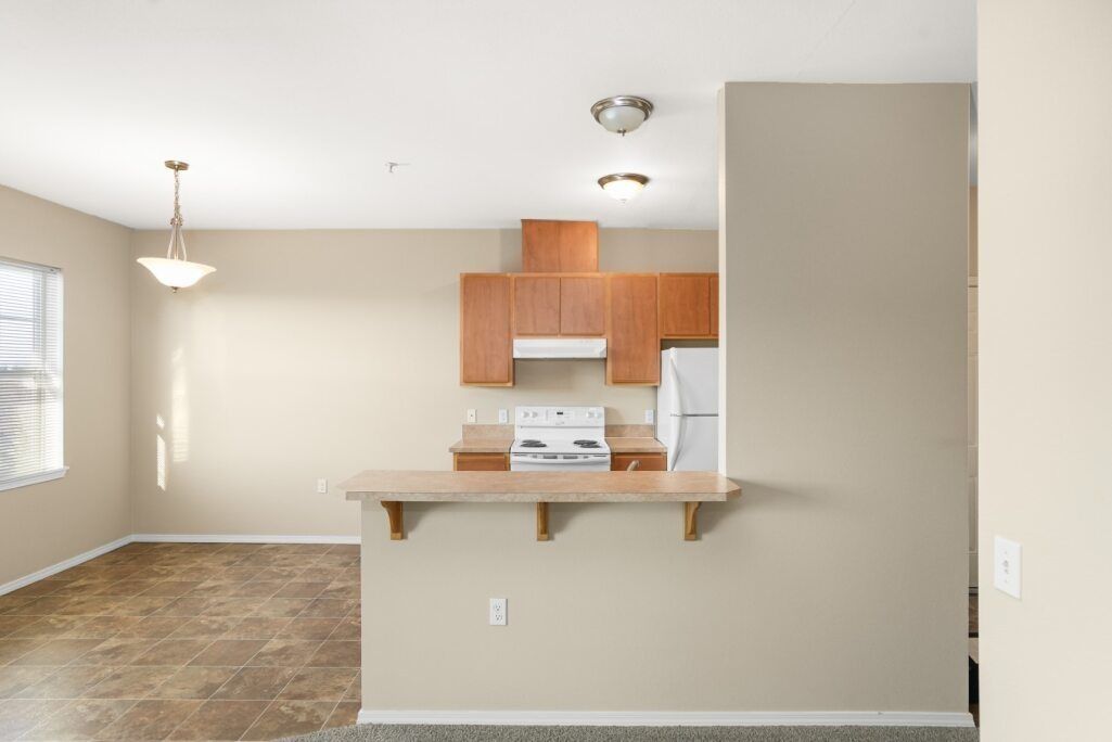 Empty beige apartment interior with kitchen pass-through, hardwood floors, and window light