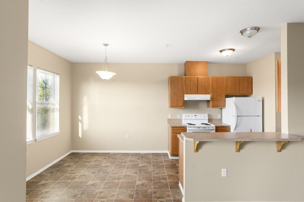 Empty kitchen and dining area with beige walls, tiled floor, and wood cabinets.