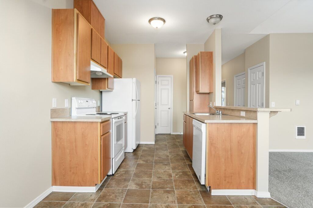 Bright kitchen with wood cabinets, white appliances, tile floor, and a small breakfast bar.