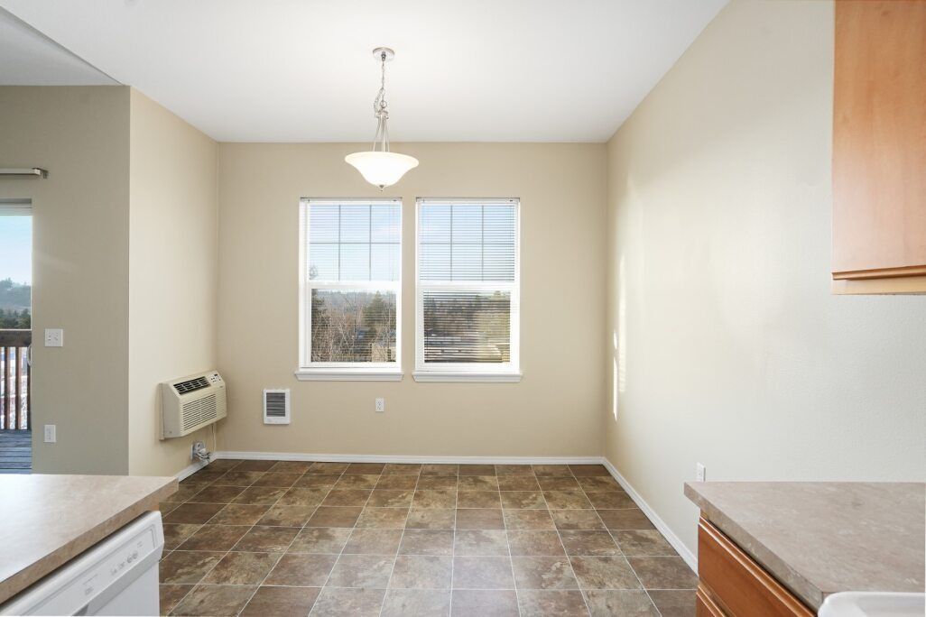 Empty kitchen nook with beige walls, tiled floor, window, and hanging ceiling light.