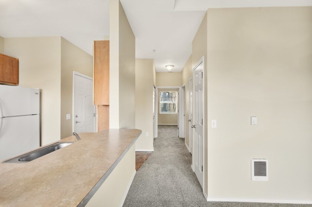 Bright kitchen view into a carpeted hallway with beige walls and a light countertop.