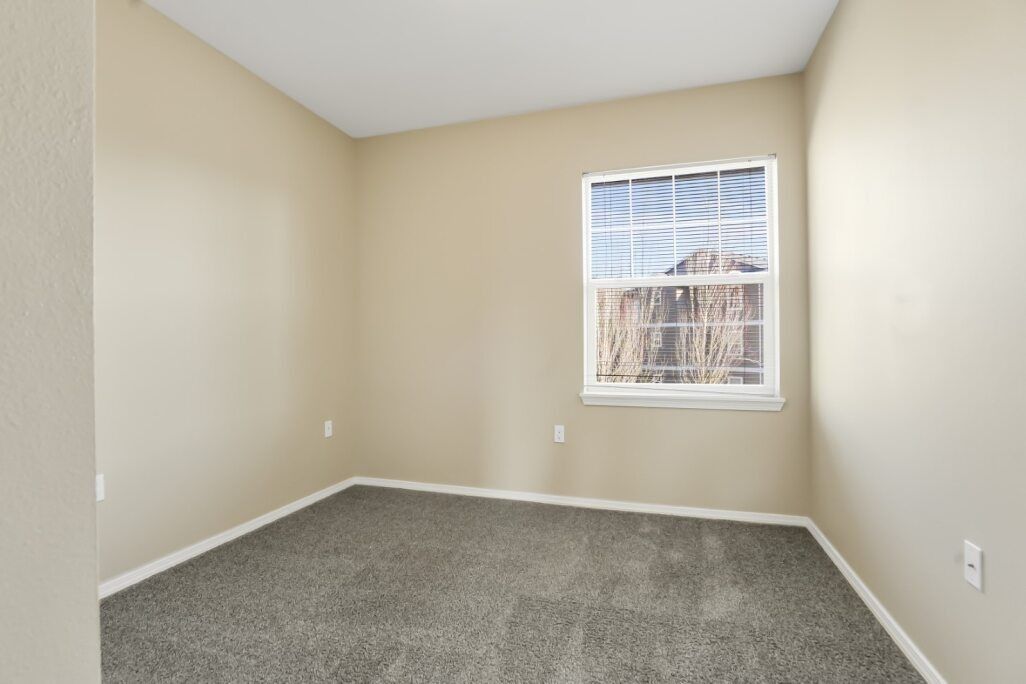 Empty beige bedroom with gray carpet and a small window