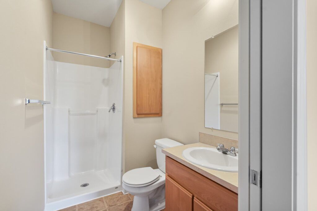 Bathroom with shower, toilet, and wooden vanity with sink in a beige interior.