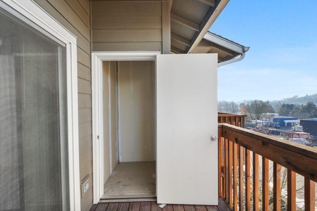 Open white door to a small outdoor storage closet on a balcony with a wooden railing and mountain view.