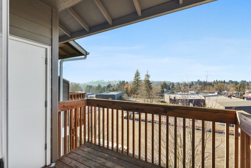 Covered wooden balcony overlooking open fields and trees under a clear blue sky