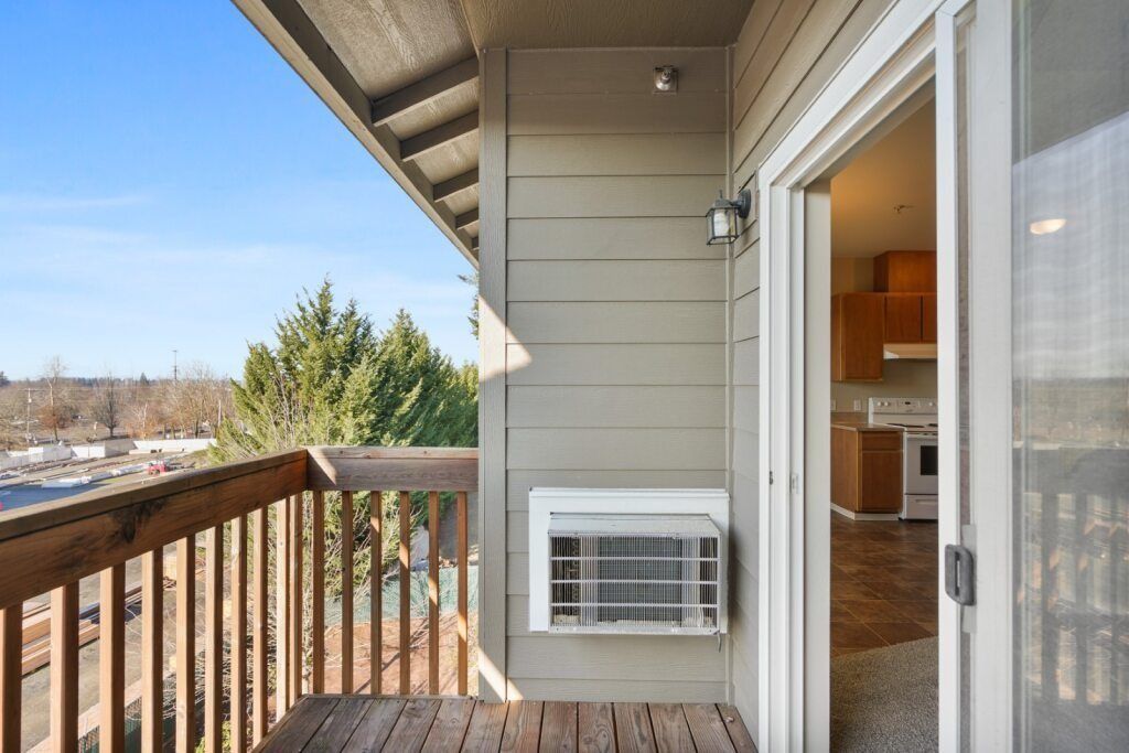 Balcony with wooden railing, wall-mounted AC unit, and sliding door to a kitchen indoors