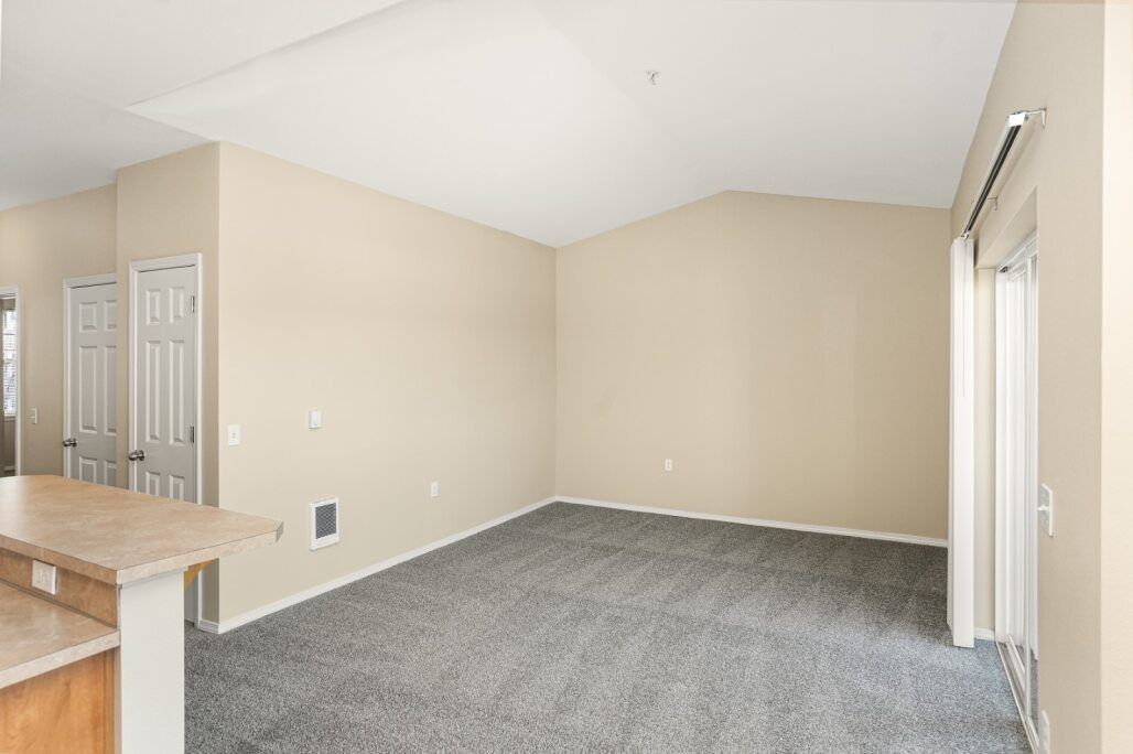 Empty beige living room with gray carpet and white double doors near a kitchen counter