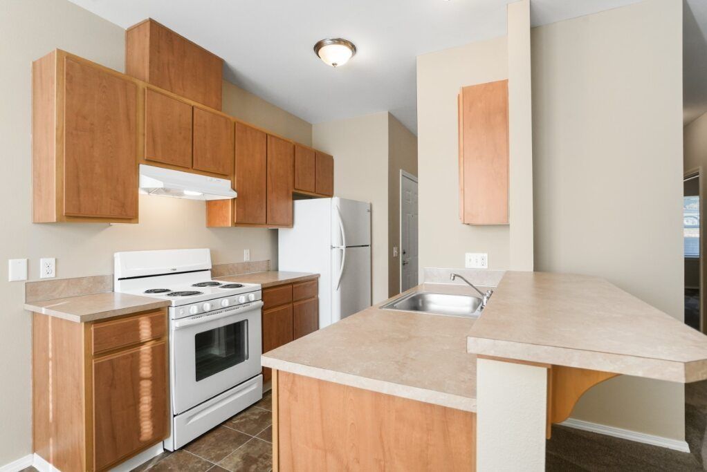 Compact kitchen with wood cabinets, white stove and fridge, and a beige countertop peninsula