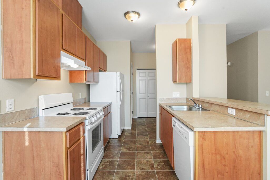 Empty kitchen with wood cabinets, white appliances, and granite countertops