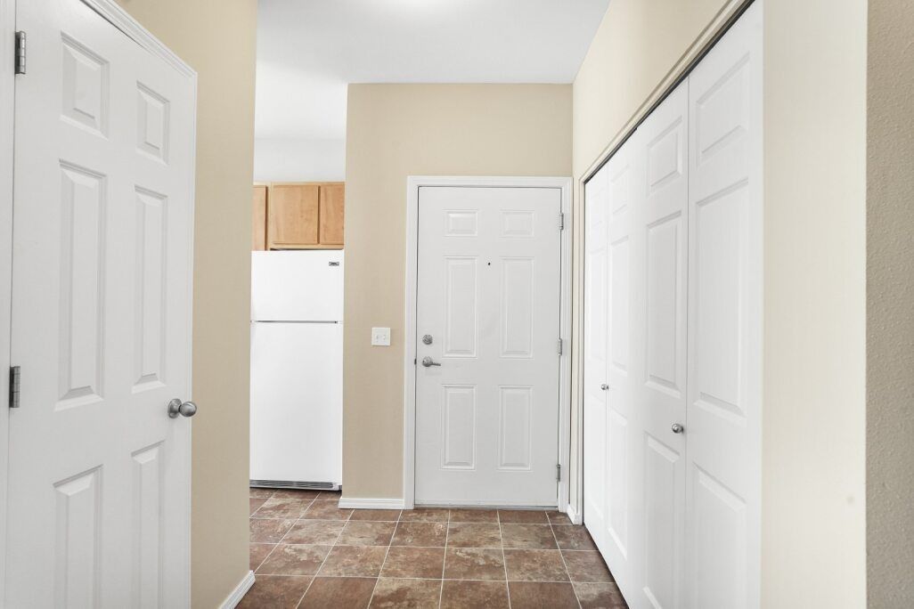 Bright hallway with white doors, beige walls, and a brown tiled floor.