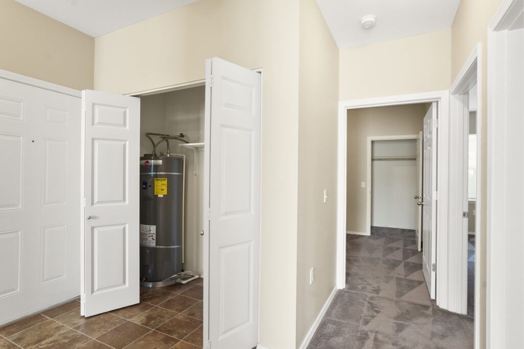 Bright hallway with open closet doors and a closet on the left, beige walls, and gray carpet.