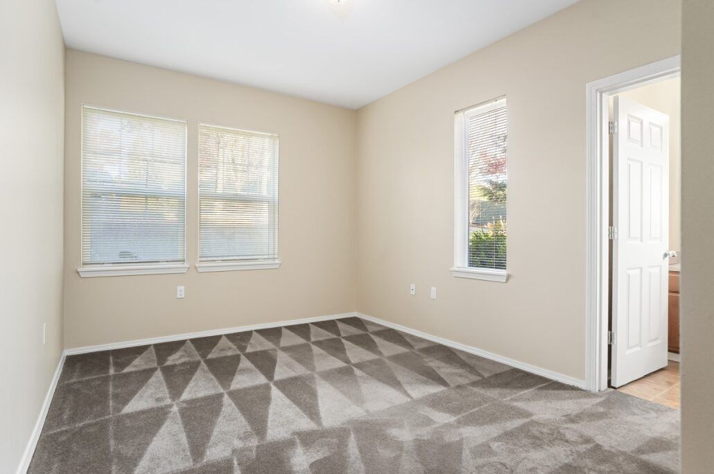 Empty beige bedroom with carpet, two windows, and an open doorway