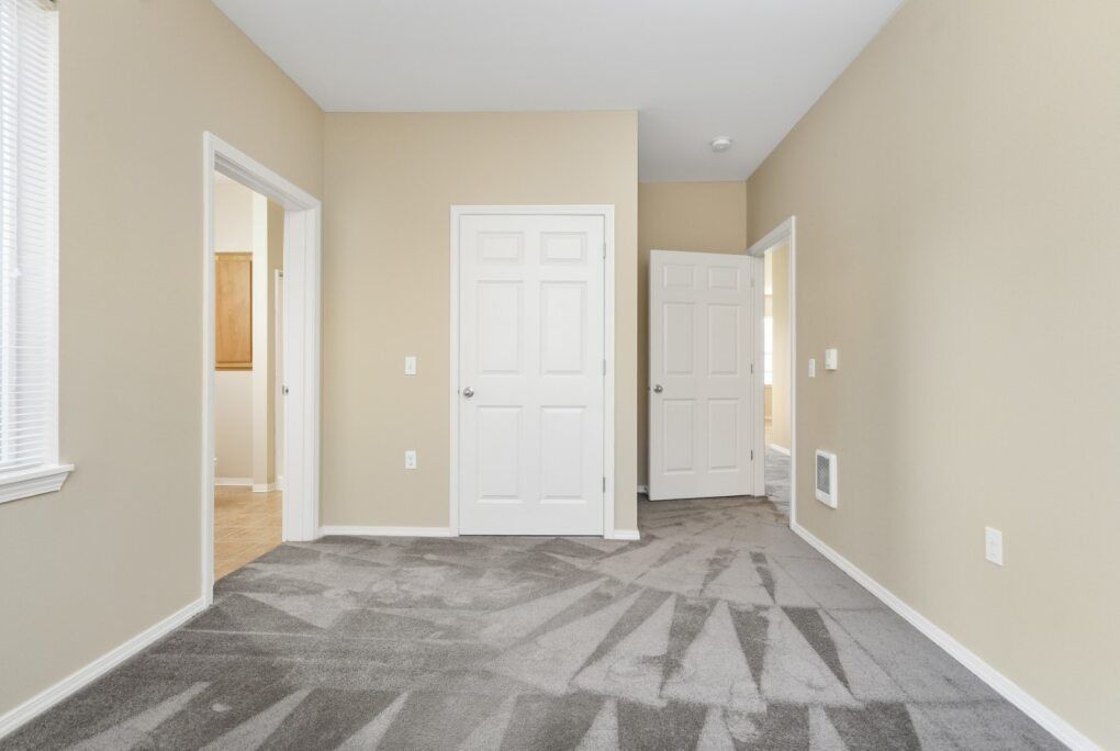 Empty beige bedroom with white doors and gray carpet flooring