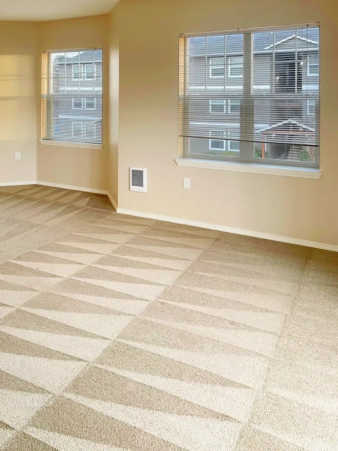 Empty beige room with carpet and two windows with white blinds.
