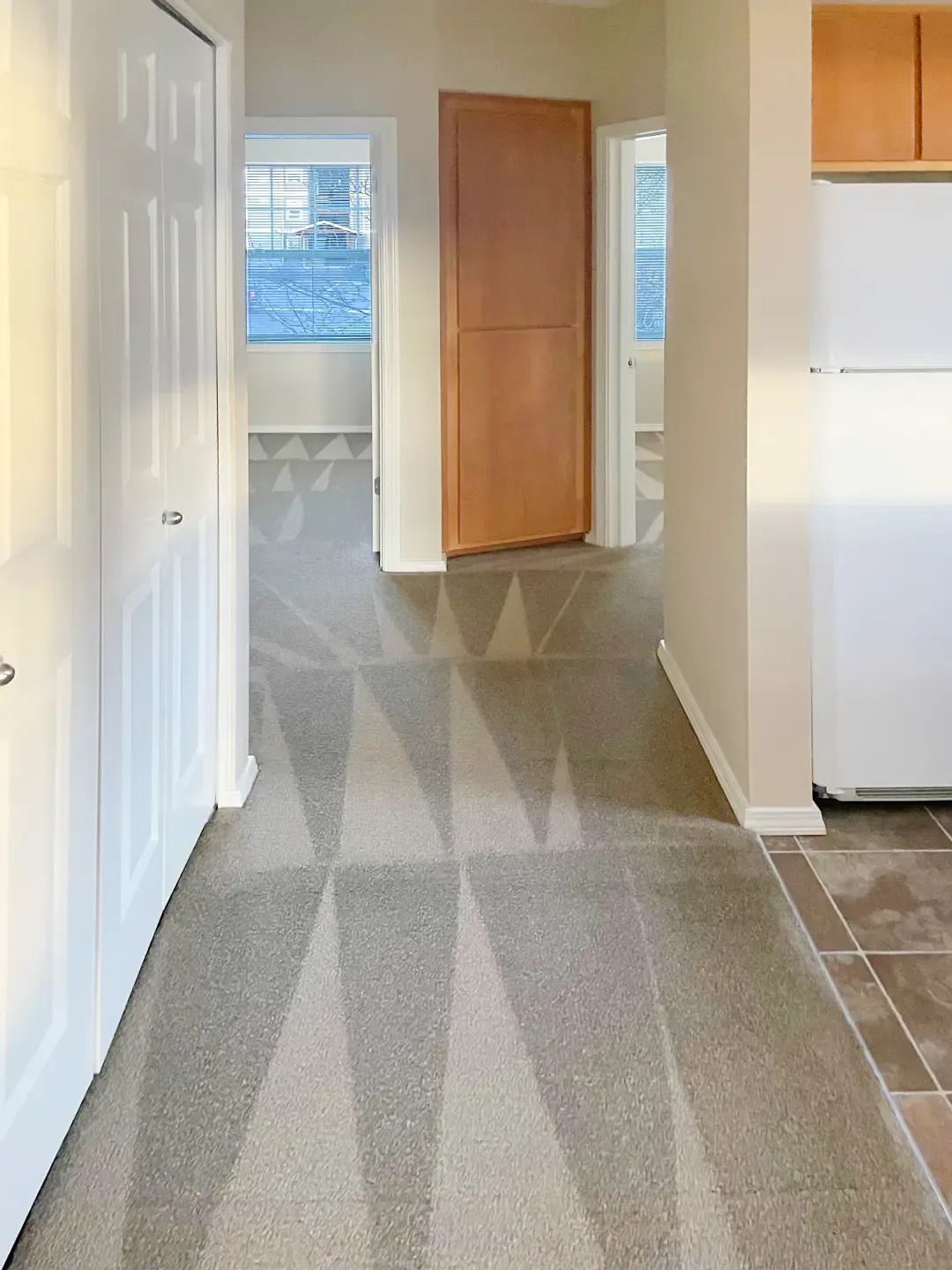 Narrow hallway with gray carpet, white walls, wood cabinet, and windows at the end.
