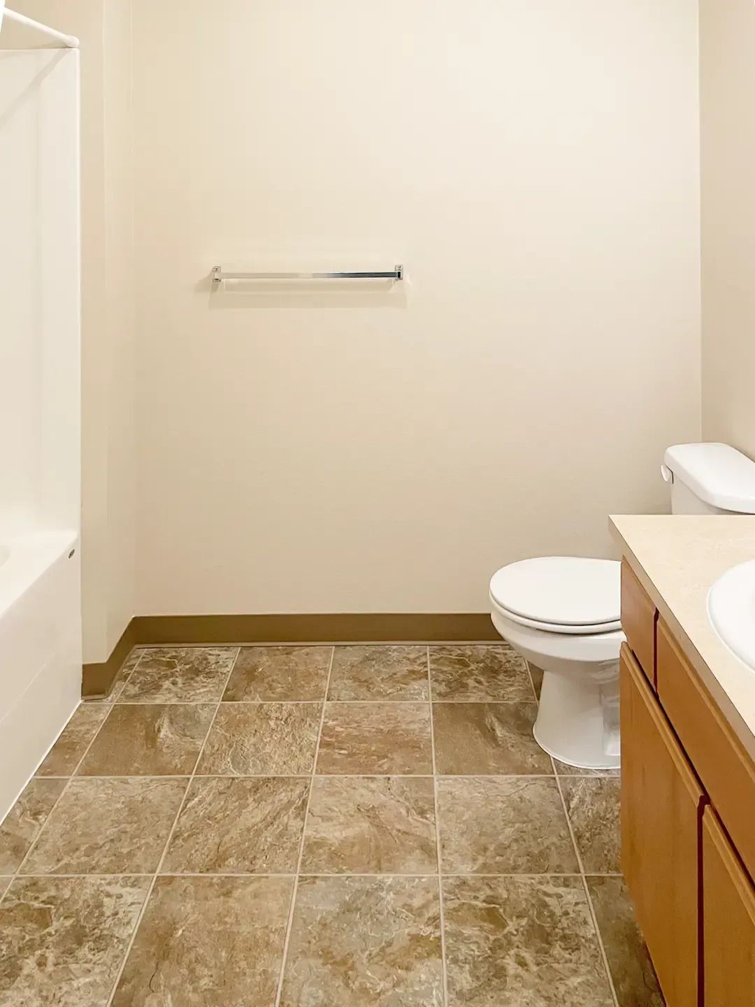Empty beige bathroom with tiled floor, toilet, towel bar, and vanity cabinet.