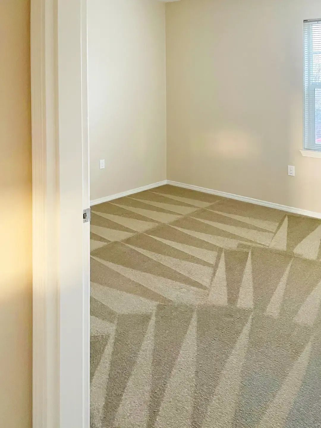 Empty beige room with patterned carpet and a window on the right.