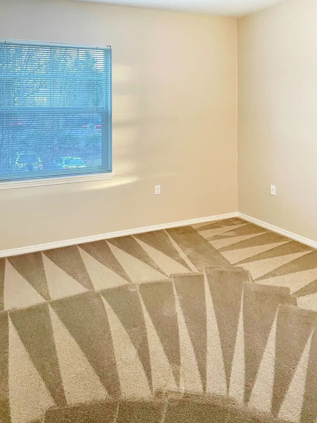 Empty beige room with patterned carpet and a window with blue blinds