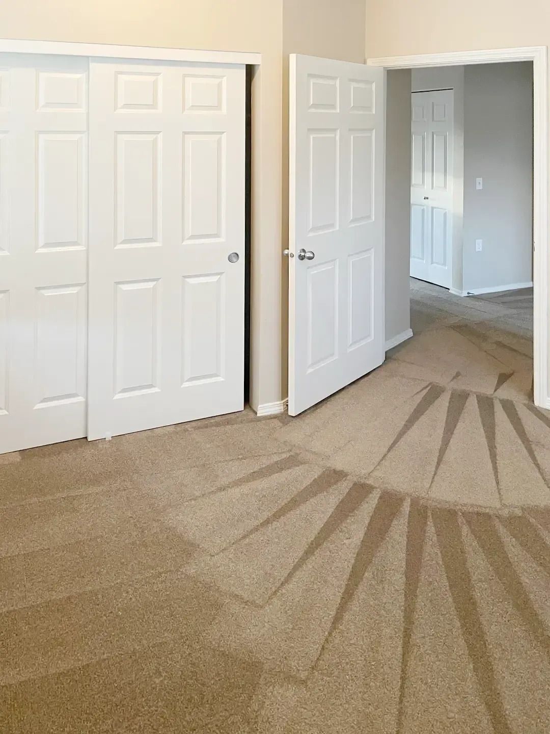 Empty beige bedroom with open white closet doors and carpeted floor.