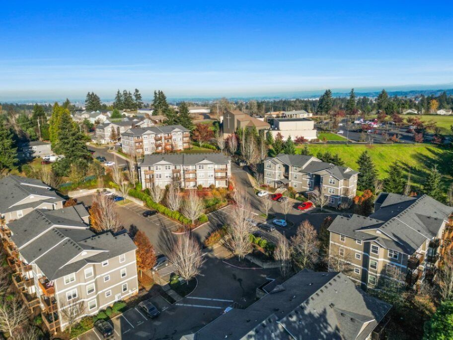 Aerial view of a suburban neighborhood with apartment buildings, trees, and distant ocean under a clear sky