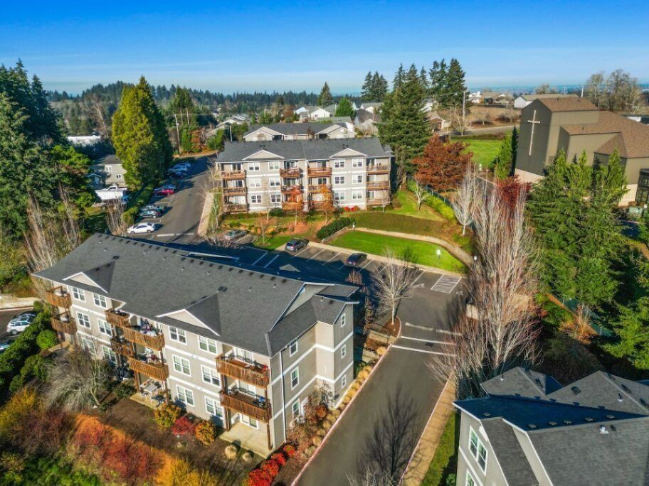 Aerial view of apartment buildings, parking lot, and trees in a suburban neighborhood