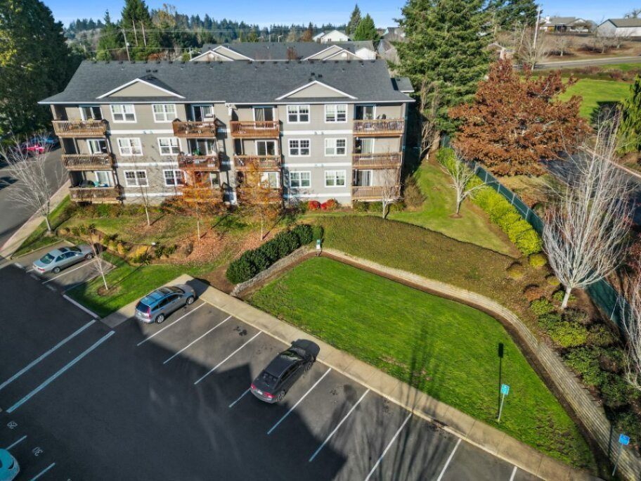 Aerial view of an apartment building beside a parking lot and green lawn with trees nearby