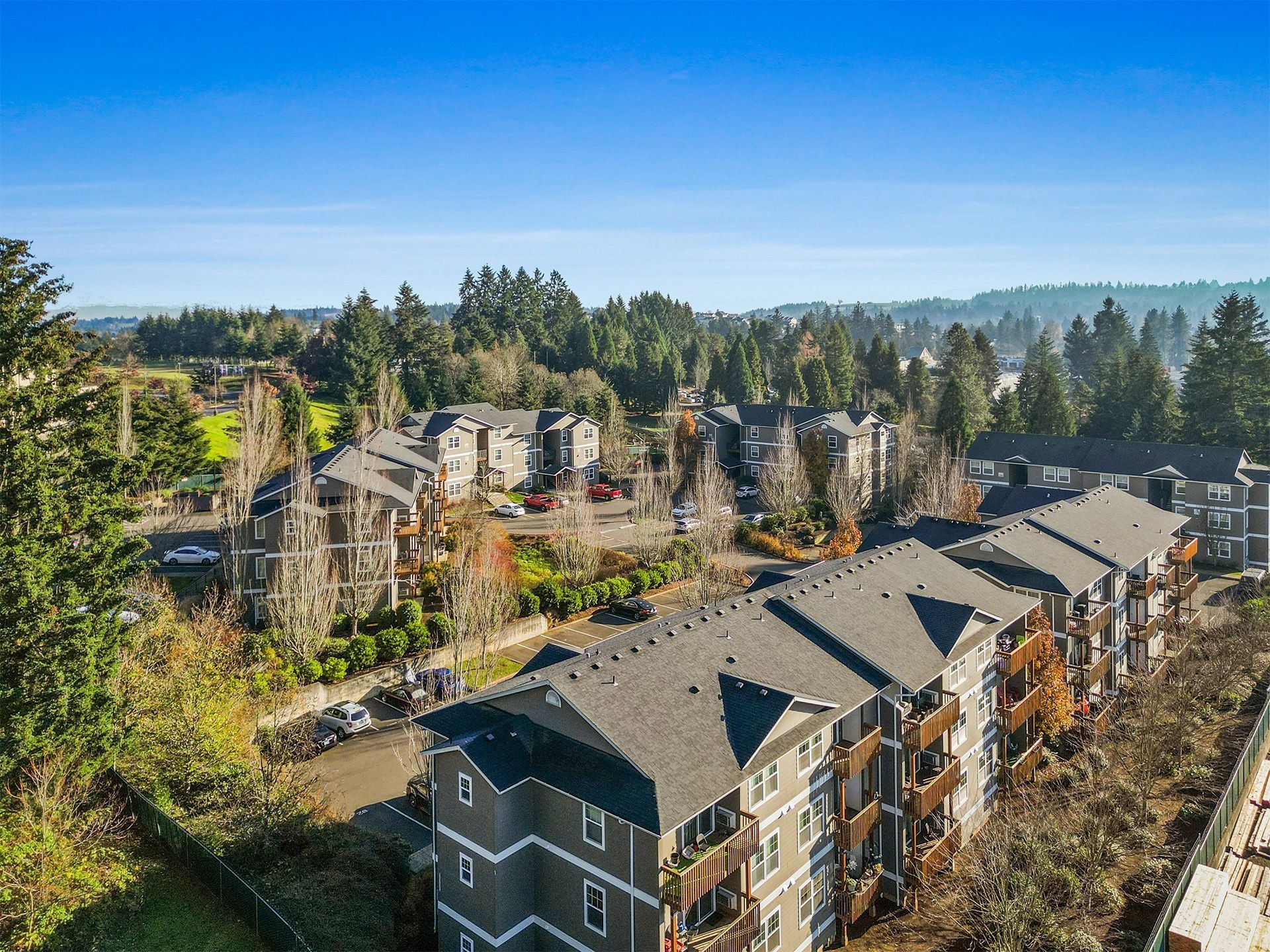 Modern apartment buildings among trees under a clear blue sky, viewed from above
