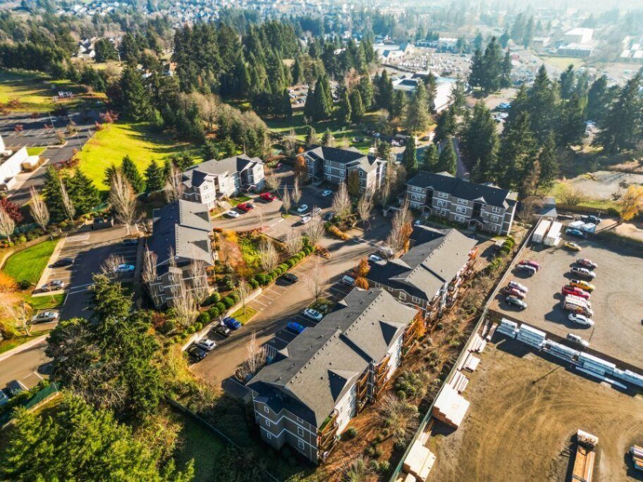 Aerial view of a large campus with gray-roofed buildings, trees, roads, and parked cars