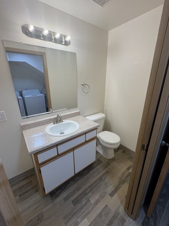 Small bathroom with sink vanity, toilet, mirror, and wood-look floor.