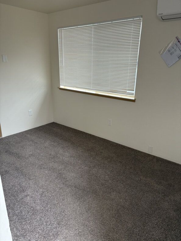 Empty beige room with gray carpet and a window with white blinds