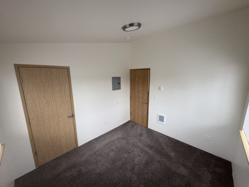 Empty beige bedroom with carpet, two wooden doors, and a wall vent.