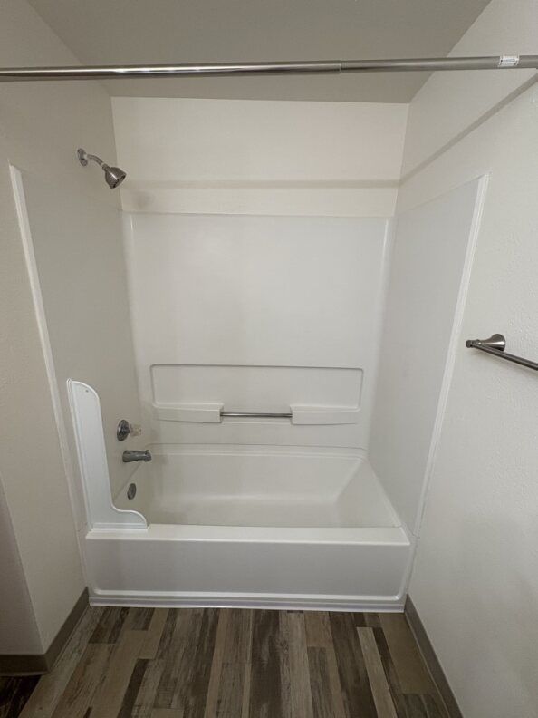 Empty white bathtub and shower area with grab bars in a small bathroom