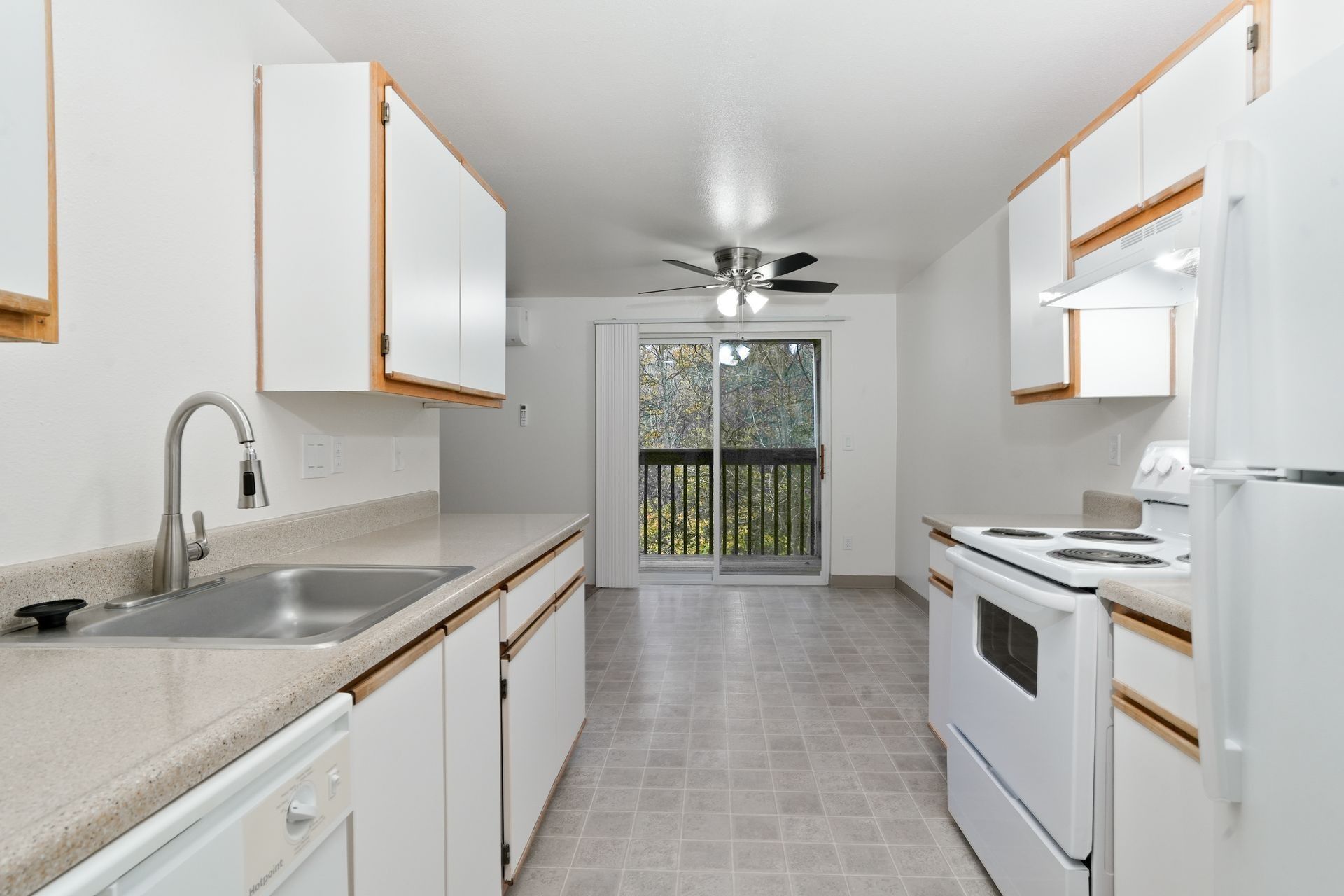 Bright white kitchen with cabinets, stove, sink, refrigerator, and a windowed dining area.