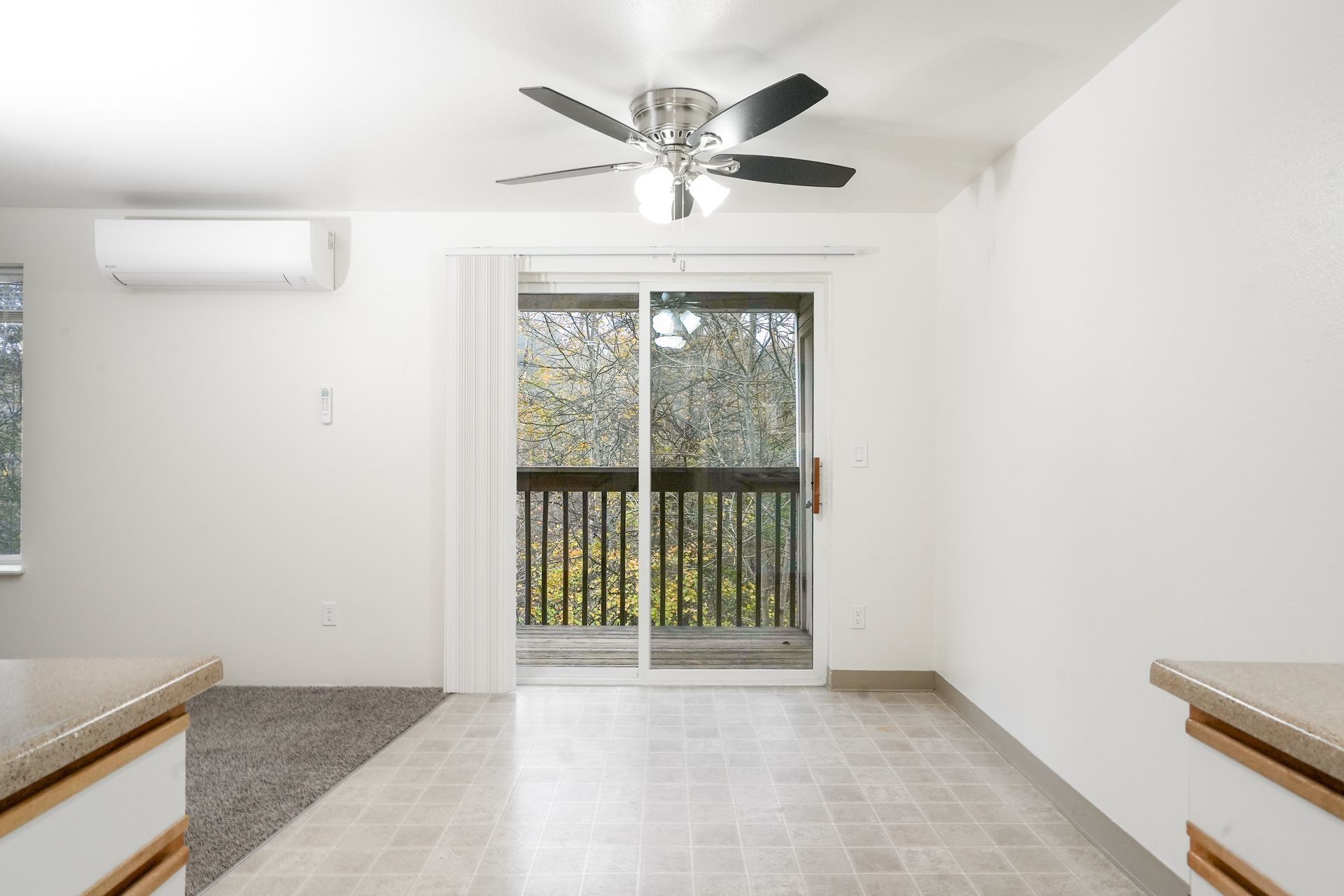 Empty bright room with white walls, ceiling fan, balcony sliding doors, and tiled floor.