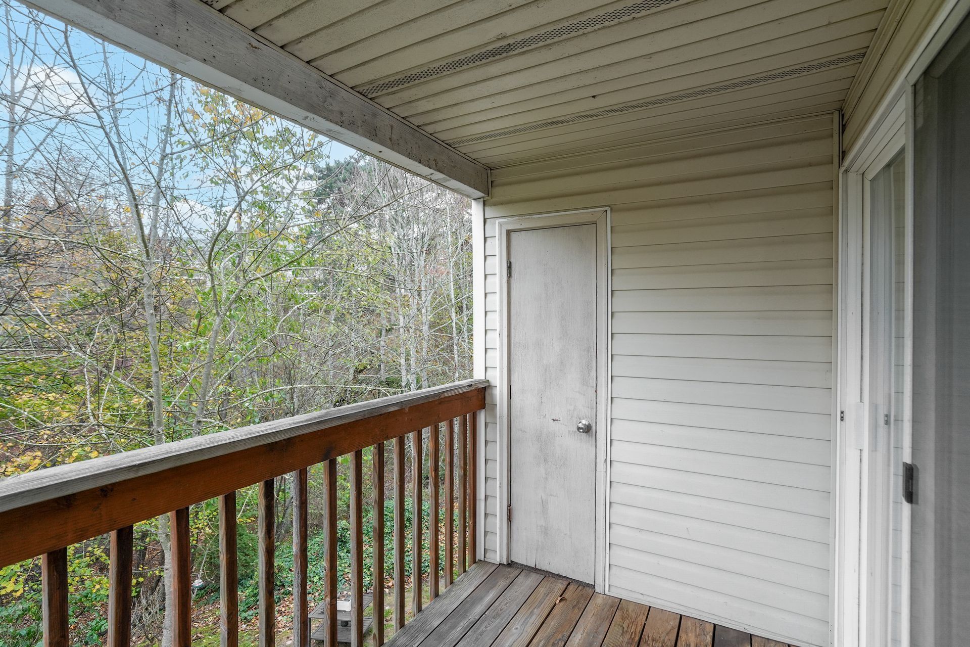 Covered porch with white siding, wooden railing, and leafless trees beyond the balcony.