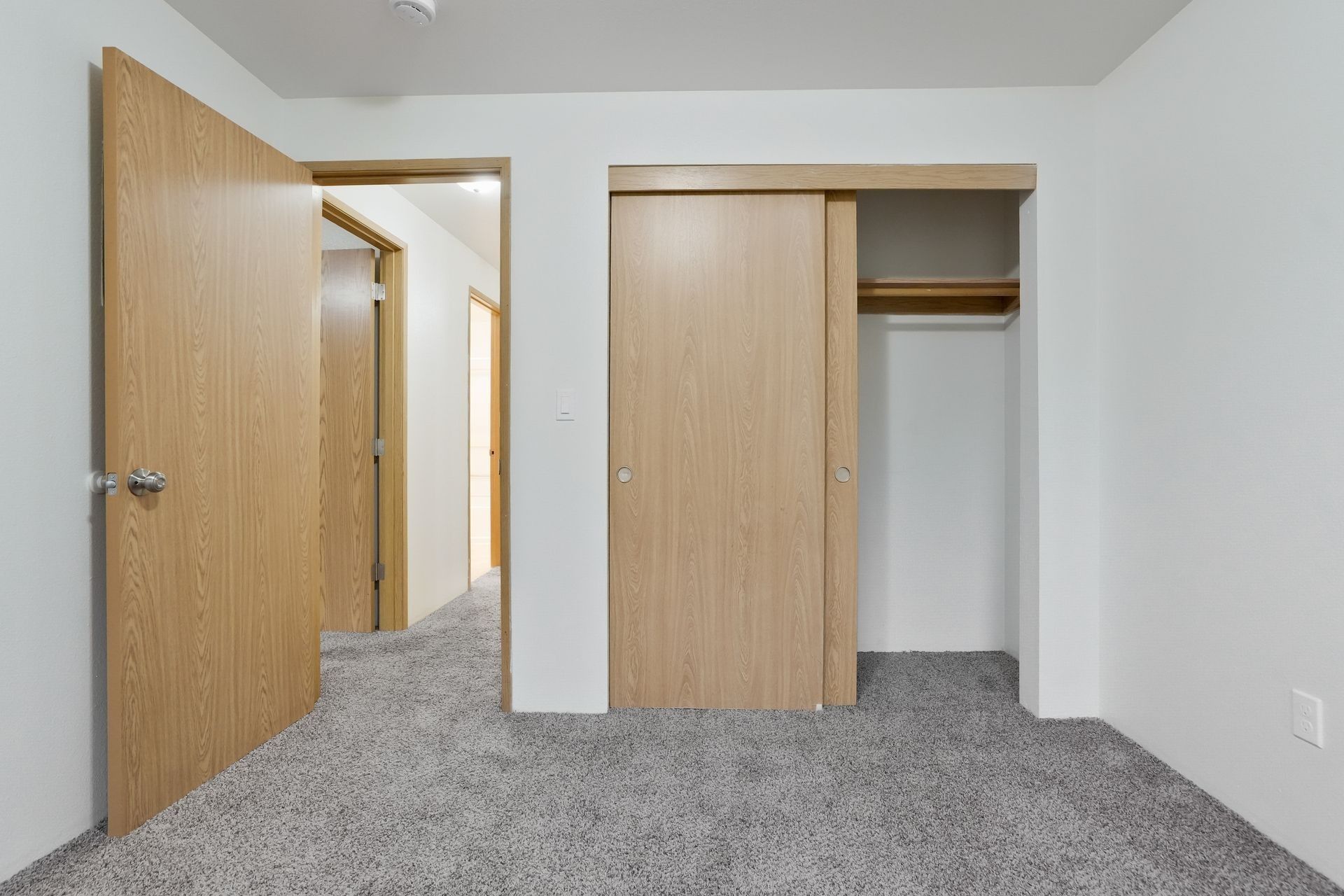Empty carpeted bedroom with open wooden doors and a closet on the right.