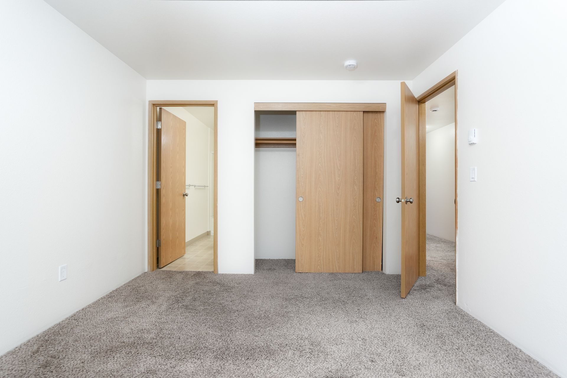 Empty bedroom with carpet, white walls, and open closet and doors.