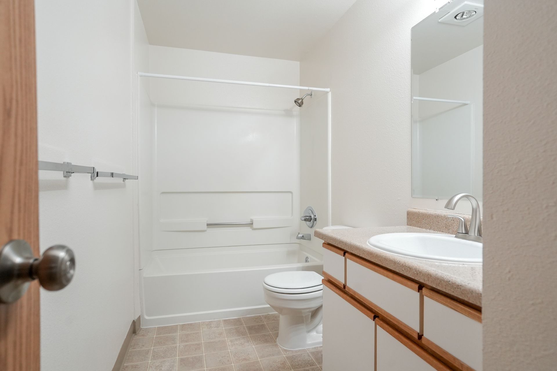 Small bathroom with white tub, toilet, vanity sink, and mirror.