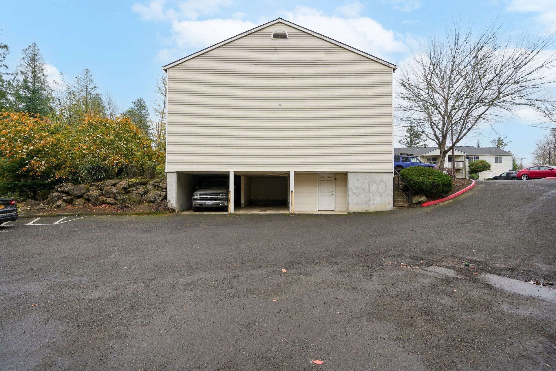 Small beige building with a driveway and parked cars on a cloudy day