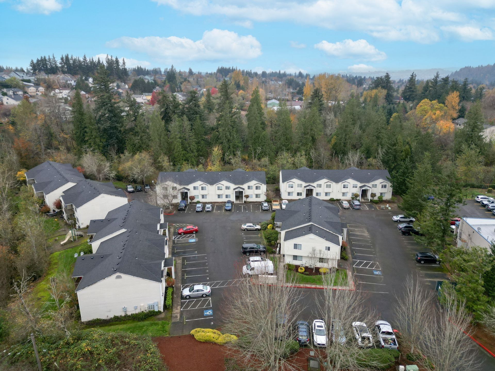 Aerial view of a residential apartment complex with parked cars and trees in autumn.