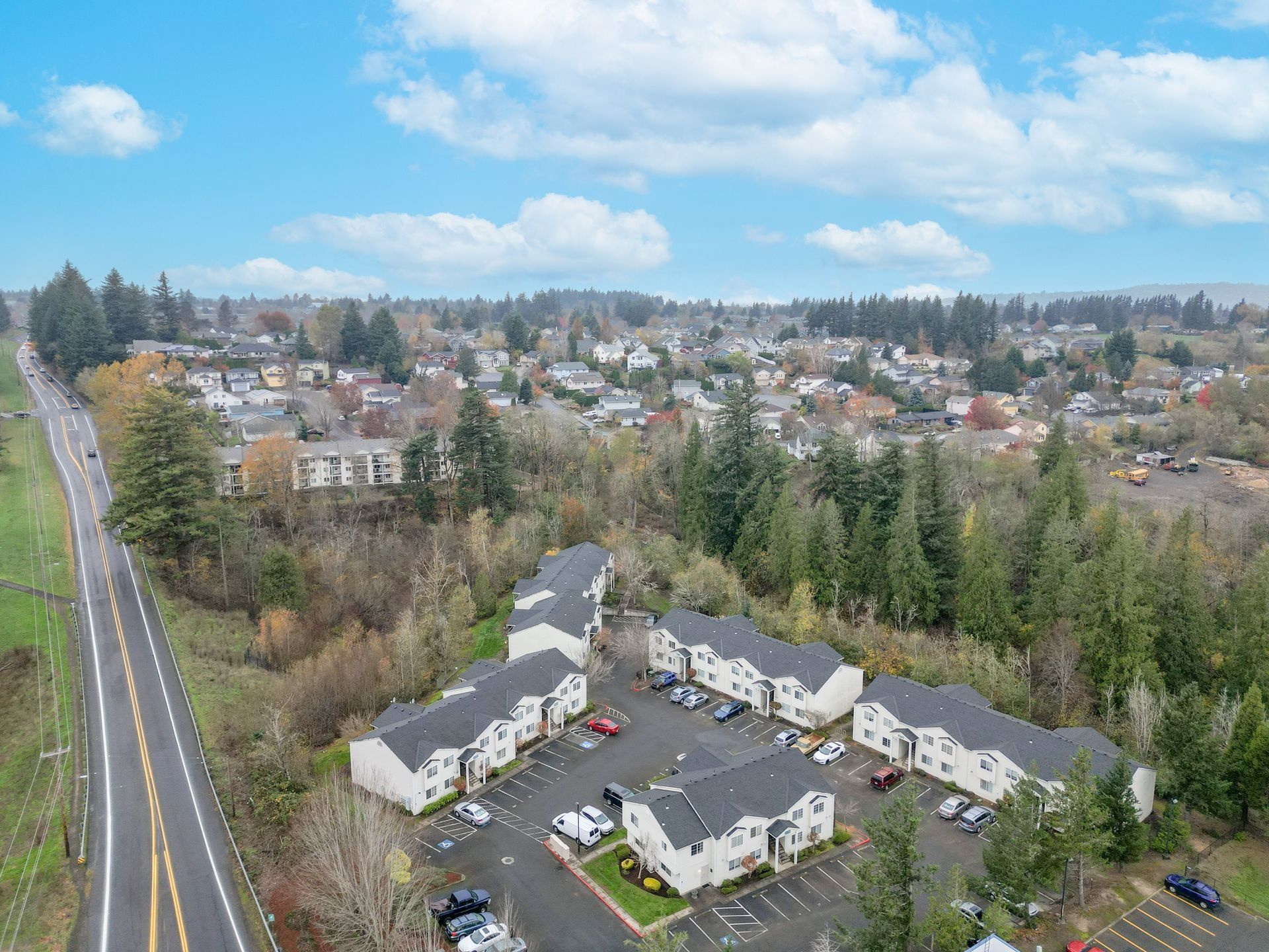 Aerial view of a suburban neighborhood with houses, trees, and a road under a blue sky