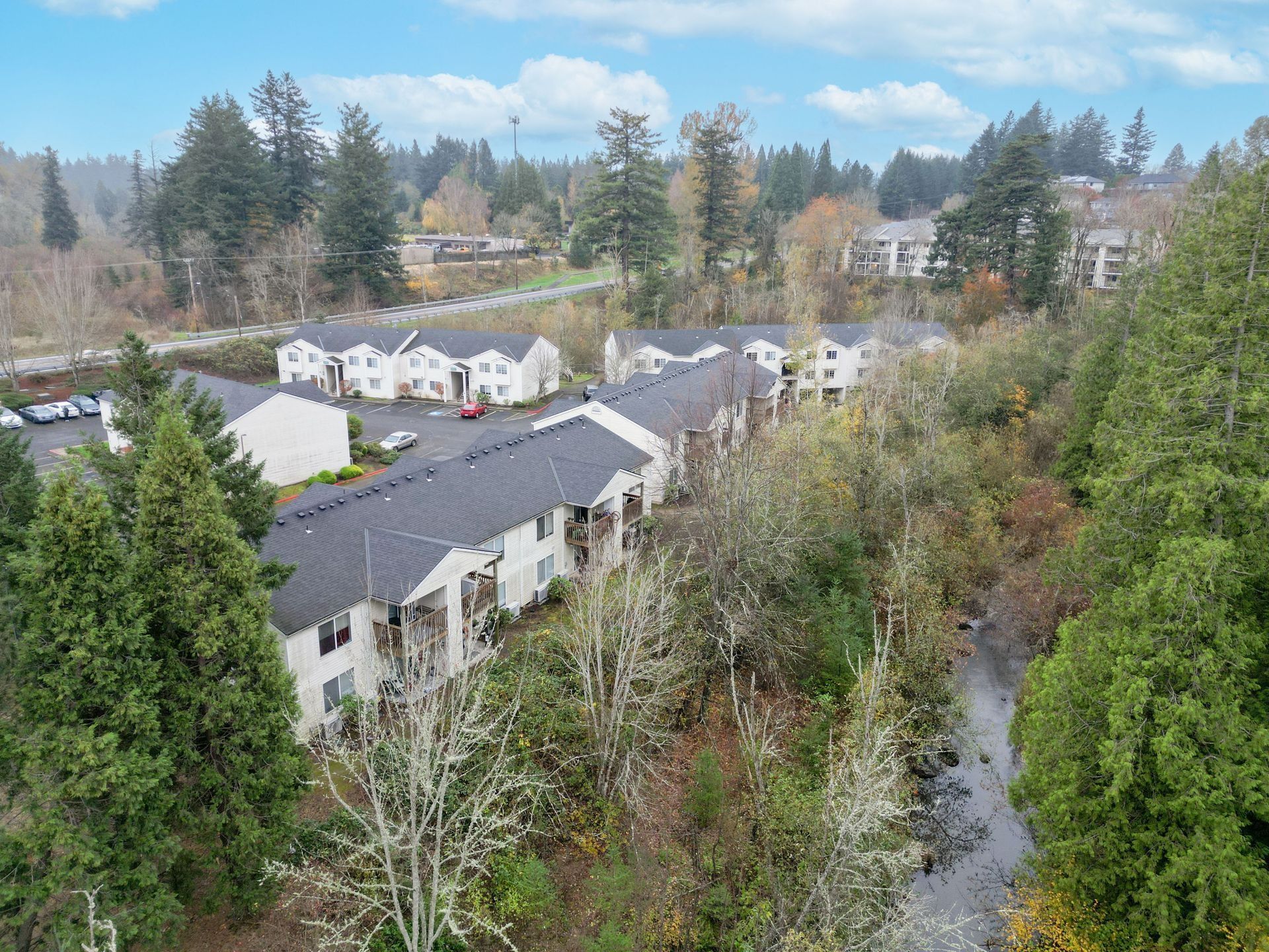 Aerial view of white townhouses beside a tree-lined creek under a blue sky
