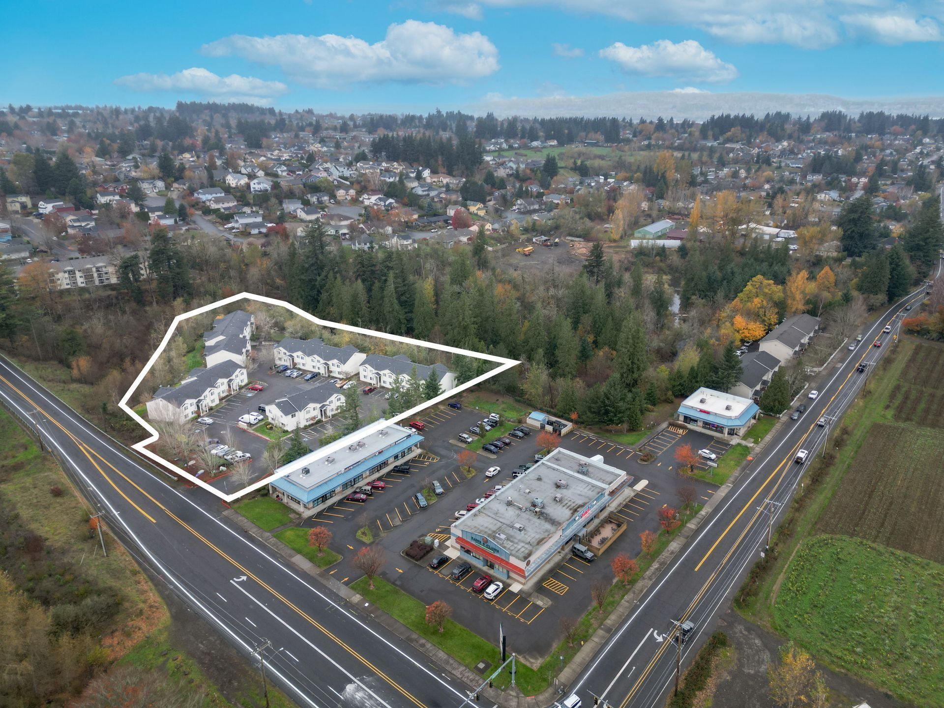 Aerial view of a suburban commercial area with roads, buildings, trees, and a highlighted white-outlined complex