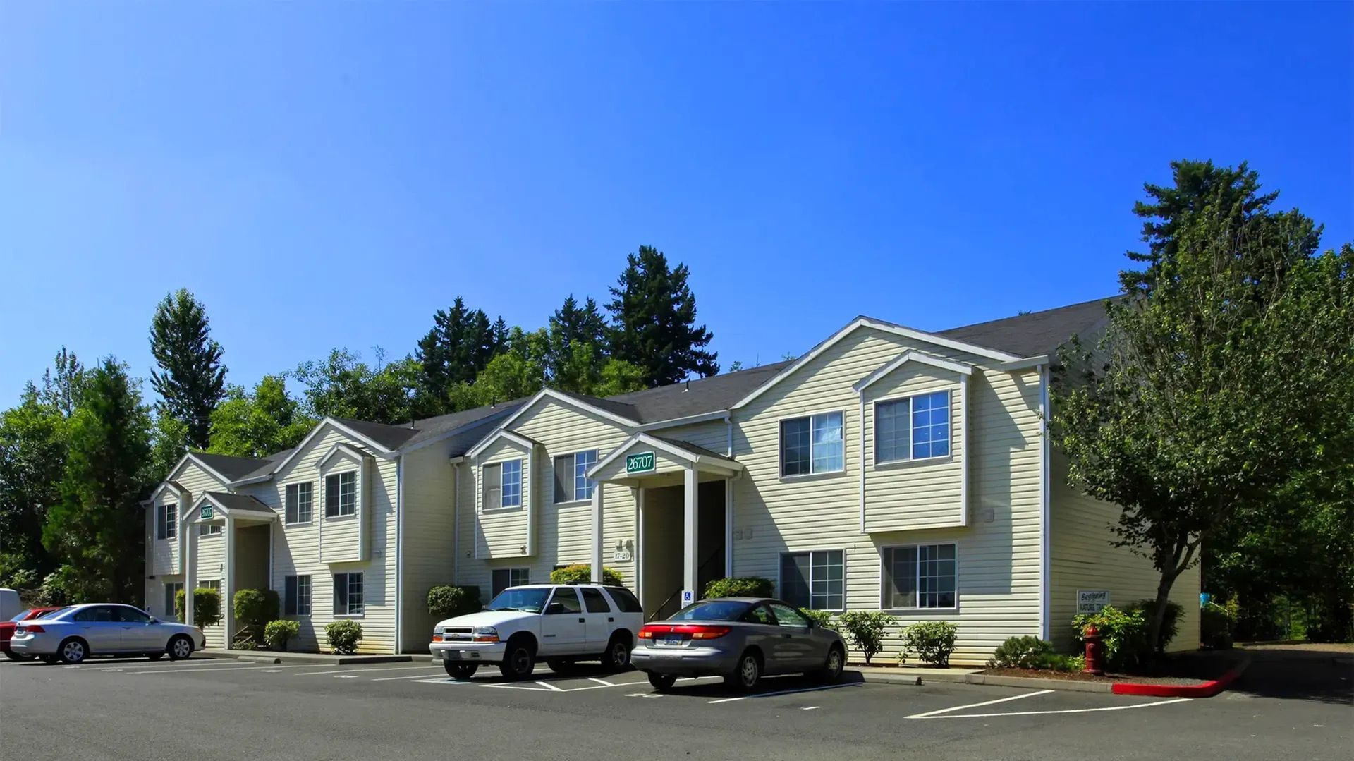 Apartment buildings with beige siding and parked cars under a clear blue sky
