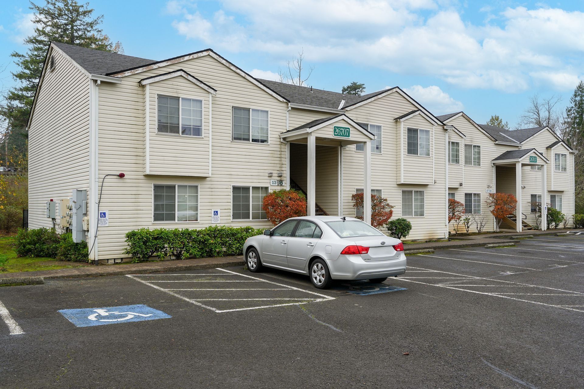 Apartment building with a parked silver car in a mostly empty parking lot.