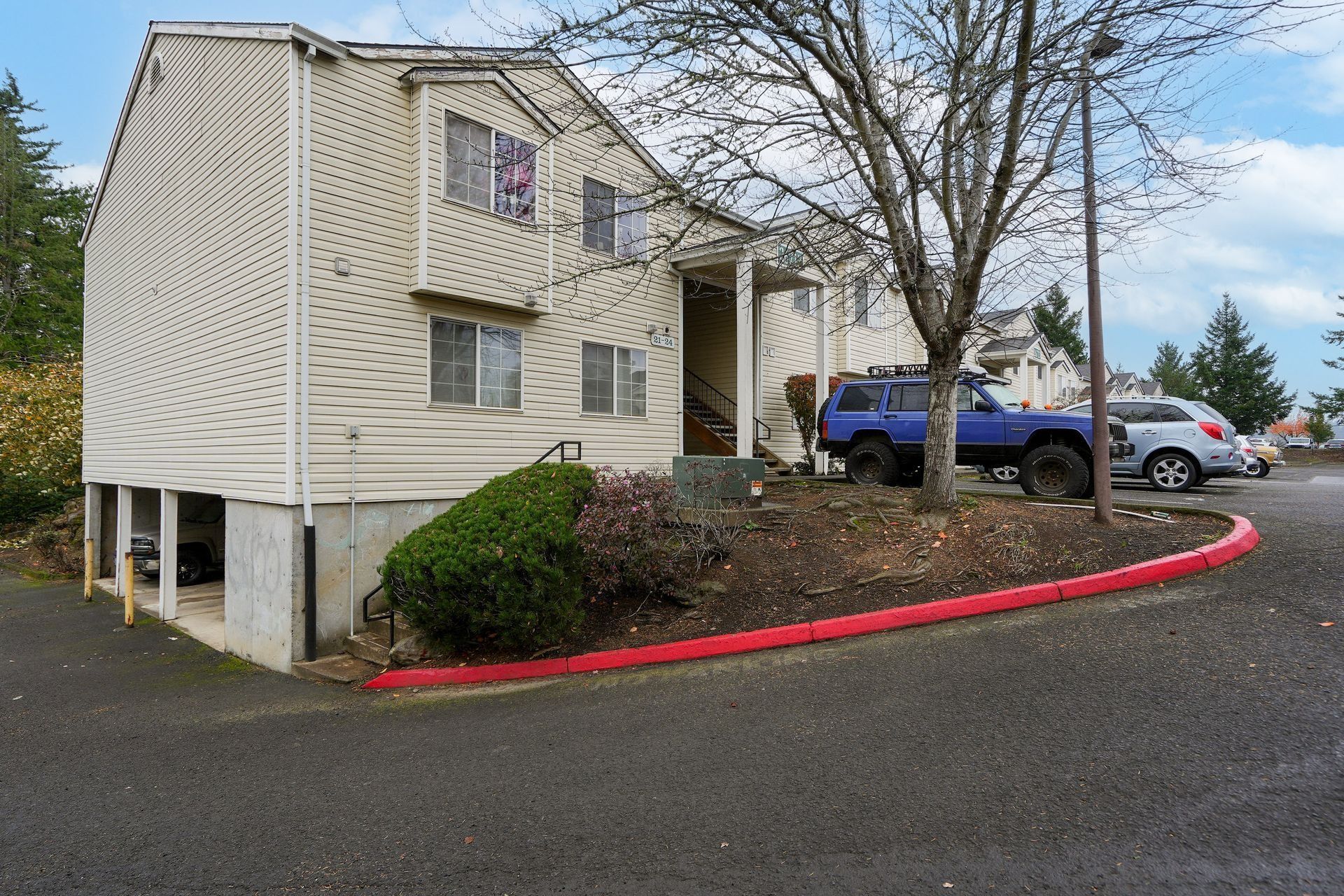 Apartment building with tan siding, blue pickup truck, and red curb in a parking lot