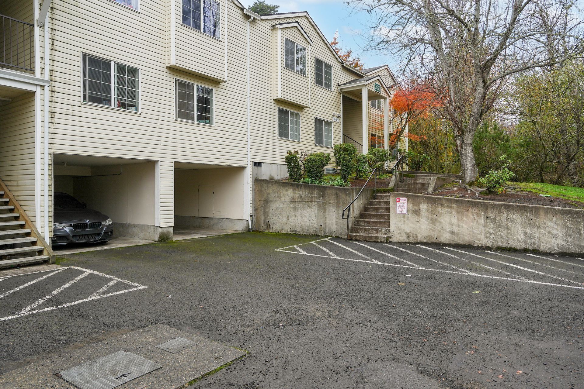 Apartment building parking area with empty spaces, a covered carport, and stairs on the left.