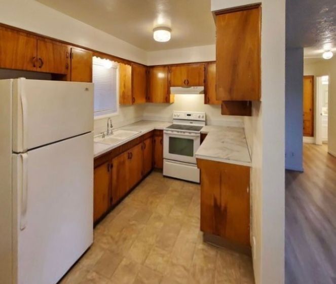 Small kitchen with white appliances, wood cabinets, and light countertops in an apartment.
